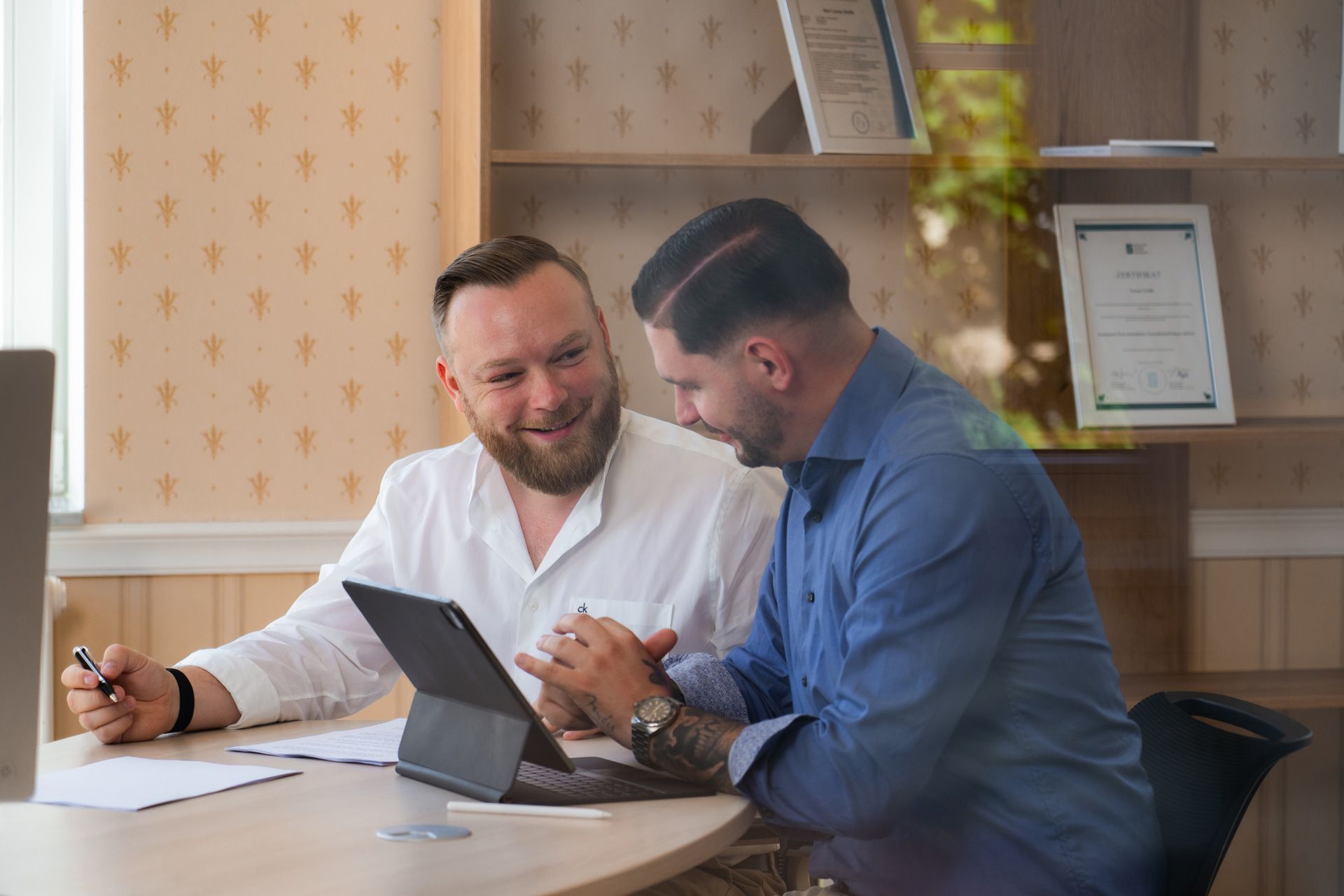 Zwei Männer arbeiten lachend gemeinsam an einem Tablet